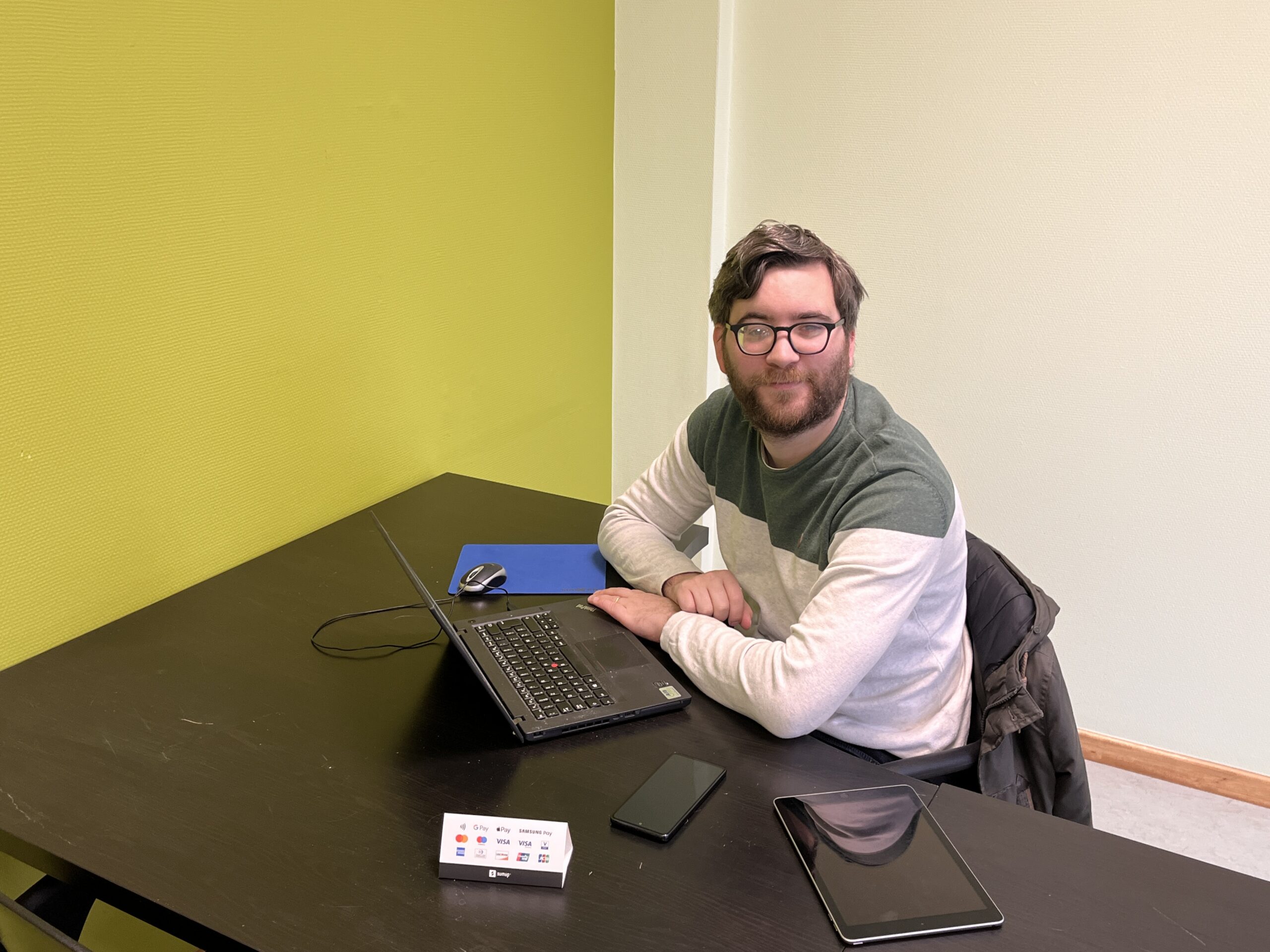 Frédéric dans un bureaux. devant lui un ordinateur, une tablette et un smartphone.